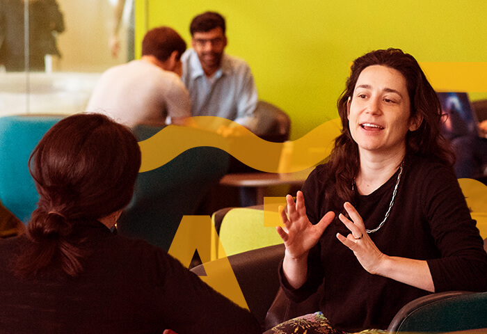 Two adults speaking to each other in a campus building. Yellow shapes have been overlaid on the photograph.